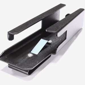 May include: A black metal clip with a rectangular body and a curved bottom. The clip has a small, light blue piece of metal attached to it. The clip is designed to hold items.