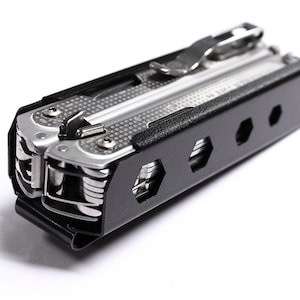 May include: A silver multi-tool with a black carrying case. The multi-tool has a variety of tools, including a knife, pliers, and a screwdriver. The case has a belt clip and a series of holes for carrying.