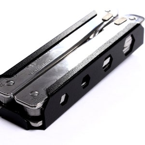 Op de afbeelding: Een zwarte multitool met een zilveren mes en een zwarte beschermhoes. De hoes heeft een zeshoekig patroon en de multitool heeft de tekst "VICTORINOX" erop gedrukt.