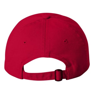 May include: A plain red baseball cap, seen from behind, with a curved peak and a fabric strap with a metal buckle for adjustment. The cap has a classic six-panel design.