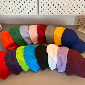 May include: A selection of baseball caps in a range of colours, such as red, orange, green, blue, pink, and black. The caps are displayed in rows, highlighting their diverse shades. The hats are made of a soft material and have a classic design.
