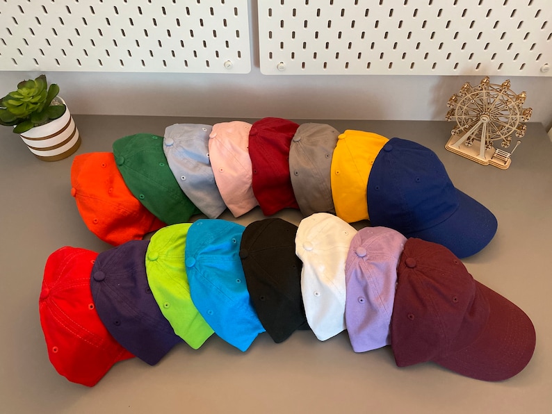 May include: A selection of baseball caps in a range of colours, such as red, orange, green, blue, pink, and black. The caps are displayed in rows, highlighting their diverse shades. The hats are made of a soft material and have a classic design.