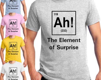 Op de afbeelding: Een grijs T-shirt met een wit periodiek systeem element ontwerp. Het element is gelabeld "Ah!" met het atoomnummer 119 en atoomgewicht 232. De tekst onder het element luidt "The Element of Surprise".