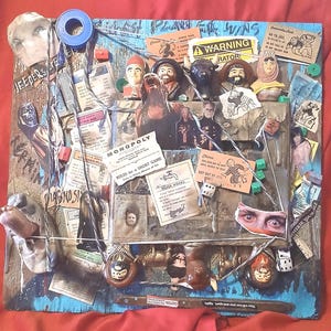 May include: A mixed-media collage on a square board featuring Monopoly game components, including property cards, a Water Works card, and a Get Out of Jail Free card. The piece incorporates small figurines, dice, string, and various cut-out images.