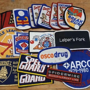 May include: A collection of embroidered patches in various shapes and sizes. Designs include baseball, a ship, and text such as "Senior", "Little League", "OSCO Drug", "Leiper's Fork", and "Spiderwire". Colors include red, blue, yellow, and white.