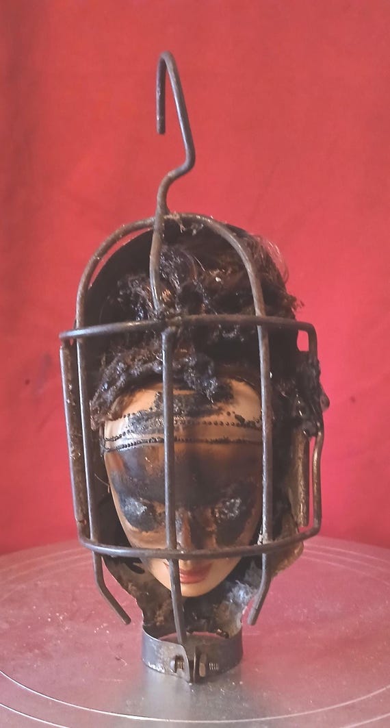 A creepy doll head encased in a cage-style light — found-object art that sits perfectly at the intersection of haunted and cool.