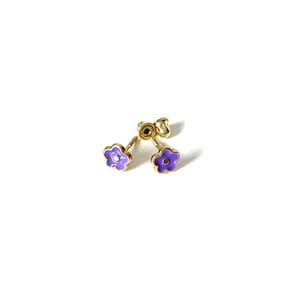 May include: A pair of gold flower stud earrings with purple enamel. The earrings have a small clear stone in the center of each flower.
