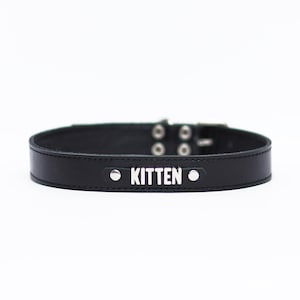 Pode incluir: Coleira de couro preto com detalhes em metal prateado e a palavra "KITTEN" gravada em prata.