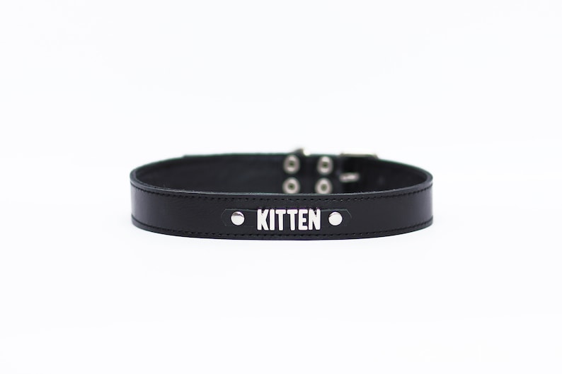 Pode incluir: Coleira de couro preto com detalhes em metal prateado e a palavra "KITTEN" gravada em prata.
