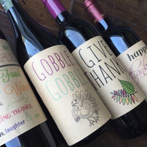 Op de afbeelding: Vier wijnflessen met bruine papieren etiketten. De etiketten hebben Thanksgiving-thema tekst en illustraties. De tekst op de etiketten luidt "Drink & Be Thankful", "Gobble Gobble", "Give Thanks" en "Happy Thanksgiving".