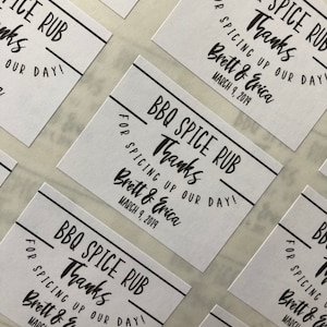 May include: White favor tags with black text that reads "BBQ Spice Rub Thanks for Spicing Up Our Day! Brett & Erica March 9, 2019".