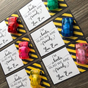 May include: Six small cards with a black and yellow striped background. Each card has a small toy car on it and the text "I'm wheelic GLAD WE ARE friends! Love, Evie".