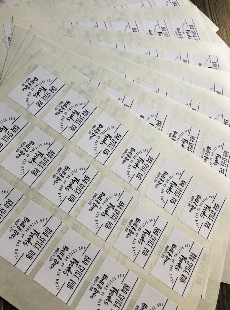 May include: A close-up of multiple white square labels with black text that reads "BBQ Spice Rub for Spicing Up Our Day! Thanks Brett & Erica"