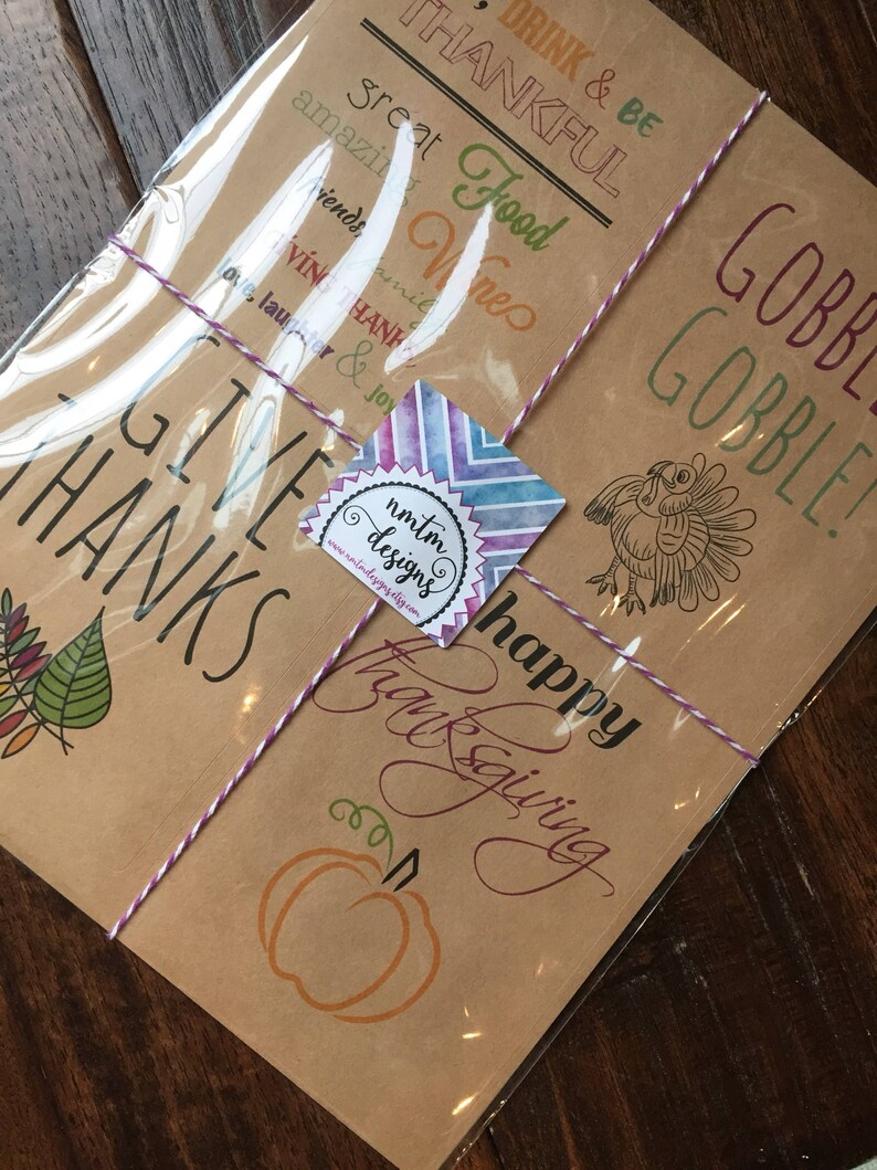 Op de afbeelding: Een set van vier bruine kraftpapierkaarten met Thanksgiving-thema illustraties en tekst. De kaarten bevatten een kalkoen, een pompoen, herfstbladeren en de woorden "Give Thanks", "Happy Thanksgiving", "Drink & Be Thankful", "Gobble Gobble" en "Great Food Wines Friends".