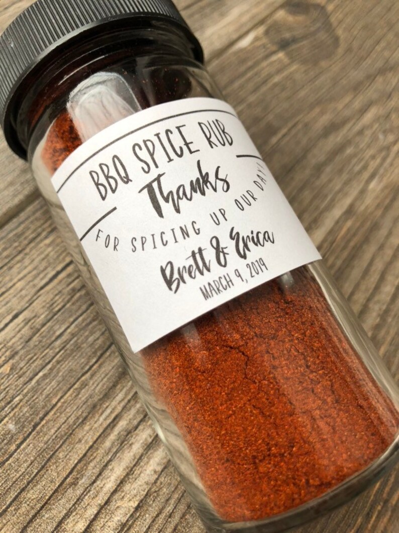 May include: A glass jar filled with red BBQ spice rub with a white label that reads "BBQ Spice Rub Thanks for spicing up our day! Brett & Erica March 9, 2019"
