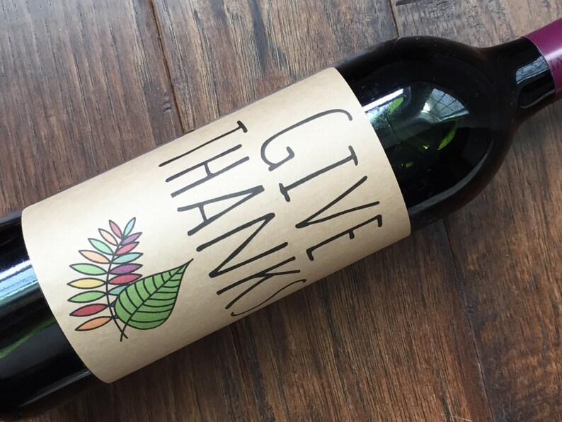 Op de afbeelding: Een bruine wijnfles met een papieren etiket waarop "GIVE THANKS" staat met een kleurrijk bladontwerp.