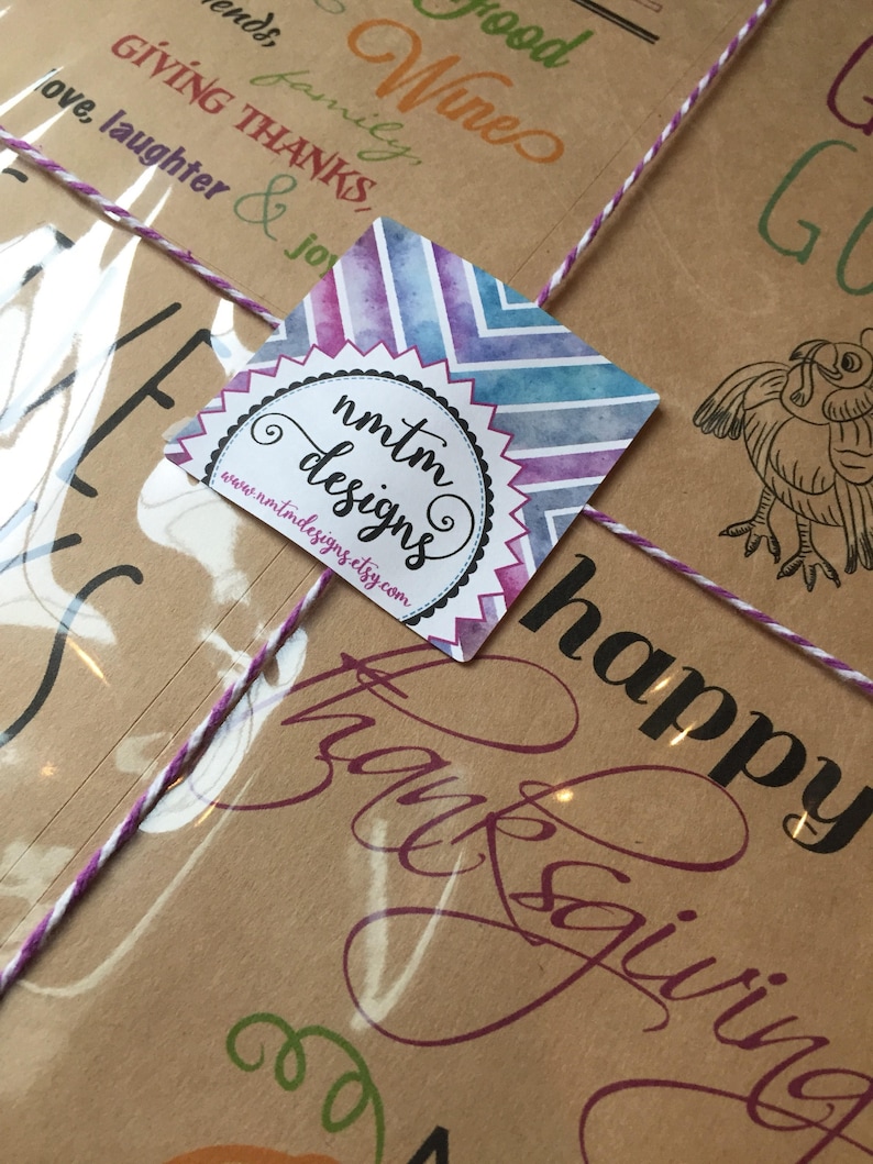 Op de afbeelding: Een bruin papieren pakketje dat vastgebonden is met touw en een paars lint. Het pakketje heeft een sticker met een aquarelontwerp en de tekst "nmtm designs" en "www.nmtmdesigns.etsy.com". Het pakketje heeft ook de tekst "happy thanksgiving" erop gedrukt.