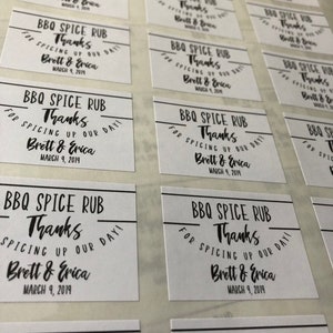 May include: White labels with black text that reads "BBQ Spice Rub Thanks for Spicing Up Our Day! Brett & Erica March 9, 2019". These labels are likely for wedding favors.