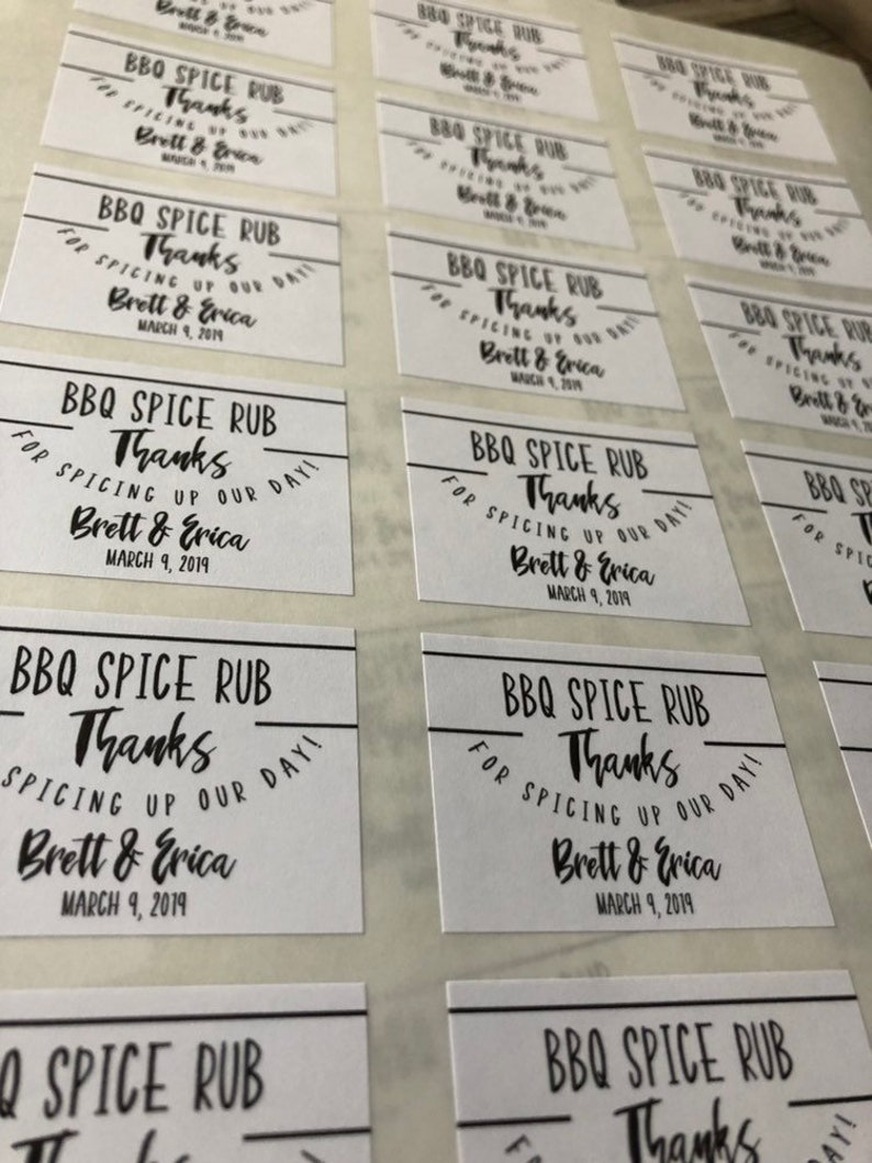 May include: White labels with black text that reads "BBQ Spice Rub Thanks for Spicing Up Our Day! Brett & Erica March 9, 2019". These labels are likely for wedding favors.