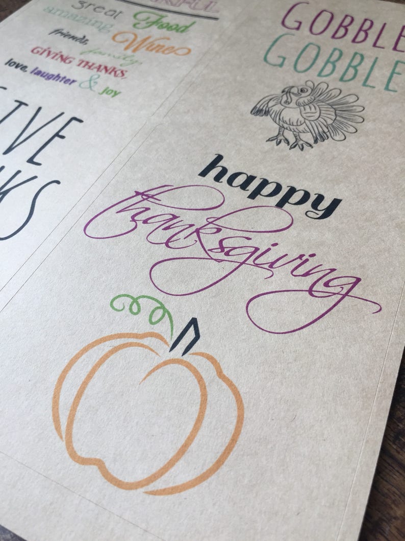 Op de afbeelding: Een bruine papieren kaart met de woorden "GOBBLE GOBBLE" in groene tekst. De kaart heeft ook een zwart-witte illustratie van een kalkoen. Onder de kalkoen staat de tekst "happy thanksgiving" in paarse en zwarte tekst. Een kleine oranje pompoen met een groene steel bevindt zich onderaan de kaart.