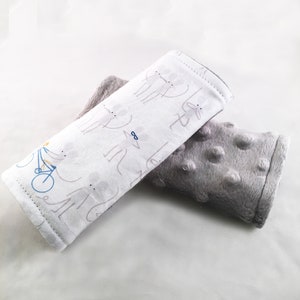 May include: A white and gray baby stroller strap with a gray and white patterned design. The strap has a gray and white polka dot pattern and a gray and white striped pattern. The strap is rolled up and the gray and white polka dot pattern is visible.