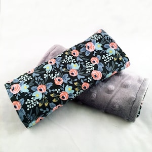 May include: Two fabric car seat headrest covers. One is black with a floral pattern and the other is gray with a textured surface.
