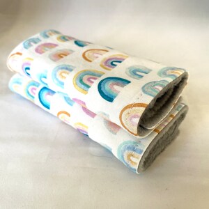 May include: Two folded white fabric burp cloths with a rainbow pattern. The cloths are made of soft, absorbent fabric and are perfect for wiping up spills and drool.