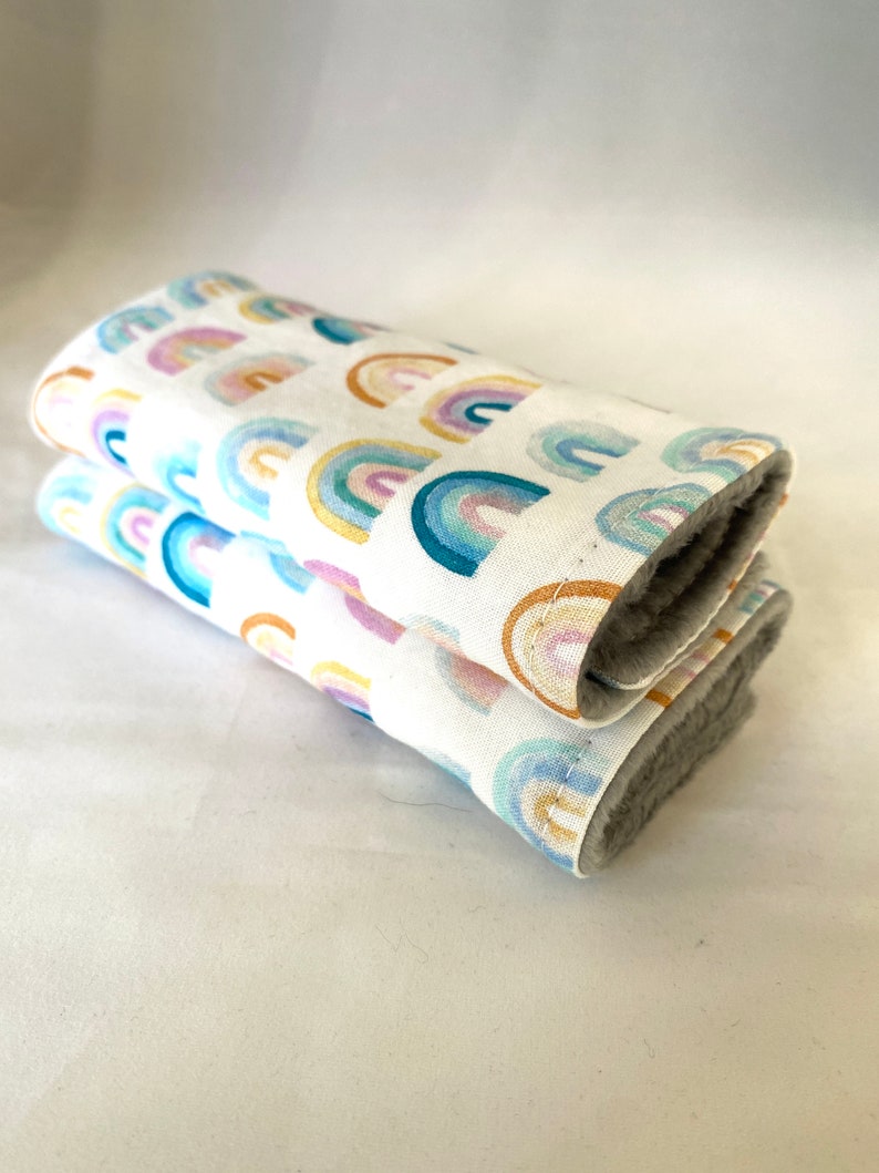 May include: Two folded white fabric burp cloths with a rainbow pattern. The cloths are made of soft, absorbent fabric and are perfect for wiping up spills and drool.