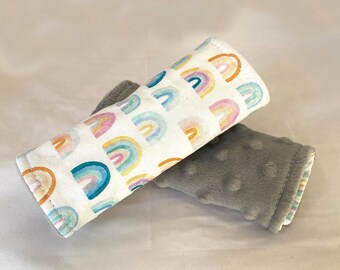 May include: Two fabric baby stroller straps. One strap is white with a rainbow pattern and the other is gray with a textured surface.