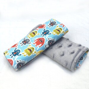 May include: A pair of car seat belt covers. One side is gray with a textured surface. The other side is blue with a pattern of colorful monsters.