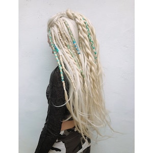 May include: Long, flowing blonde dreadlocks with turquoise and blue accents. The dreads are styled with a mix of thick and thin sections, creating a textured and unique look. The hair cascades down the back, offering a bohemian and alternative aesthetic.
