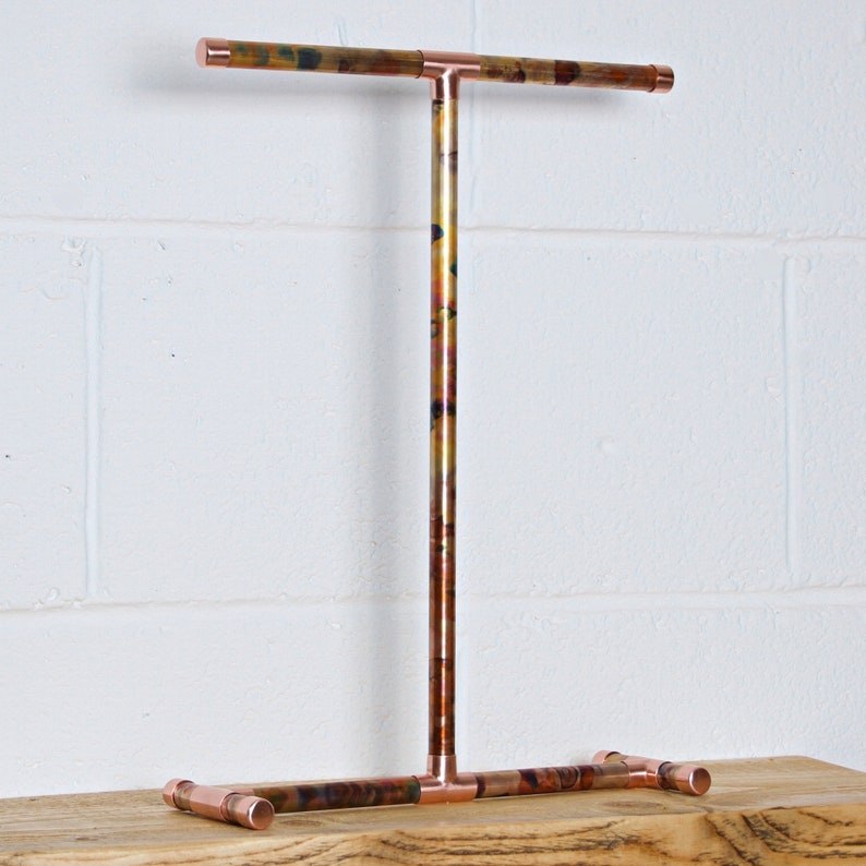 May include: A copper jewelry stand with a T-shaped top bar and a base with three legs. The copper has a mottled, multi-colored patina.