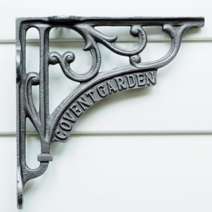 May include: A cast iron shelf bracket with an ornate design and the words "Covent Garden" inscribed on it. The bracket is painted a dark grey colour.