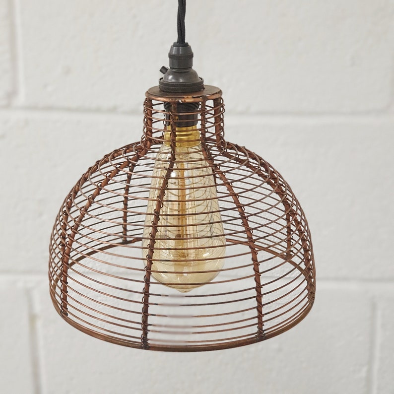 A bronze metal bell cage retro pendant hanging light shade, with a braided cord, suspended in a room, providing a warm, vintage glow.