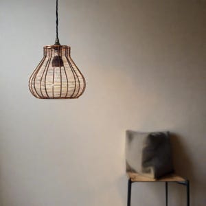 A bronze metal bell cage retro pendant hanging light shade, with a braided cord, suspended in a room, providing a warm, vintage glow.