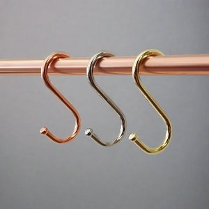 A metal rod displaying three different coloured S-hooks for utensils.