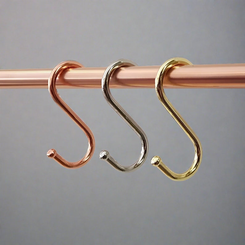 A metal rod displaying three different coloured S-hooks for utensils.