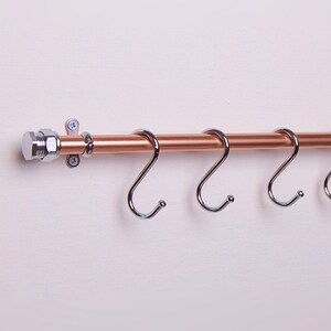 Three chrome S-hooks on a copper rail serve as a utensil rack for hanging various items.