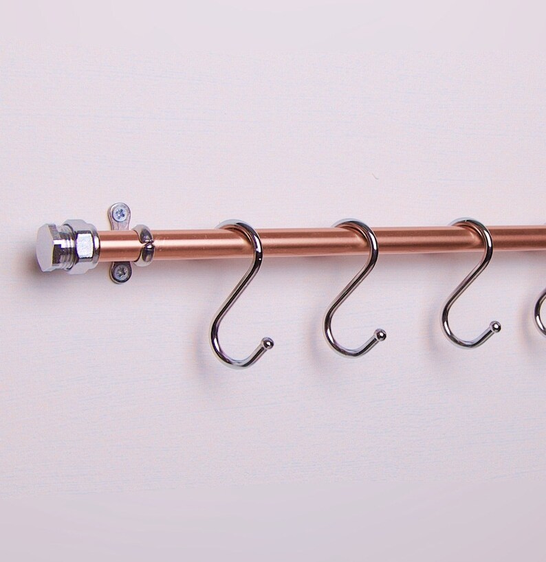 Three chrome S-hooks on a copper rail serve as a utensil rack for hanging various items.