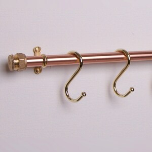 Two brass S-hooks on a copper rail serve as a useful rack for hanging various items.
