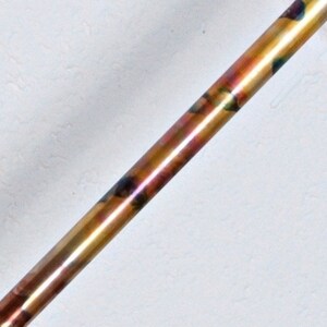 May include: A close-up of a copper pipe with a rainbow iridescent finish. The pipe is smooth and shiny.