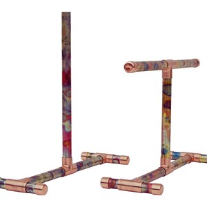 May include: Two copper pipe stands with a colorful patina finish. Each stand has a T-shaped base and a vertical pipe that extends upwards. The stands are ideal for displaying items.