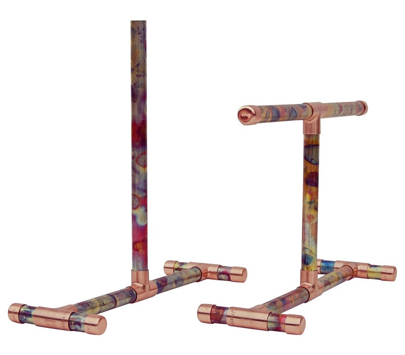May include: Two copper pipe stands with a colorful patina finish. Each stand has a T-shaped base and a vertical pipe that extends upwards. The stands are ideal for displaying items.