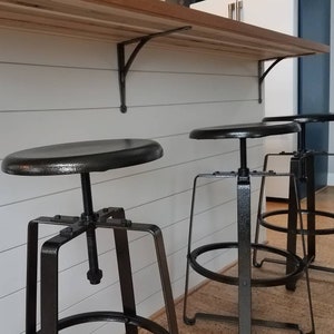 industrial themed kitchen using industrial metal stools with black cast iron shelving brackets under a wood kitchen worktop with a white panelled kitchen island.
