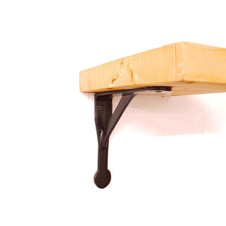 A solid cast iron shelf bracket with a satin black finish on a white wall, with a rustic wooden shelf.