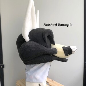 May include: Side view of a black and white fursuit head with white ears. The head is on a mannequin and the text "Finished Example" is visible in the image.