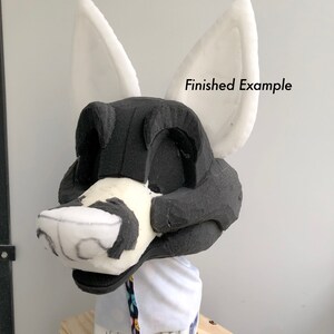 May include: A white foam base for a furry costume head, with black foam detailing and white foam ears. The base is on a wooden stand and the text "Finished Example" is visible in the image.