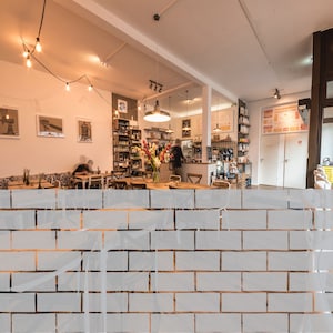 May include: A brick wall with a white frosted finish. The wall is made of rectangular bricks with a light gray mortar. The bricks are arranged in a staggered pattern.