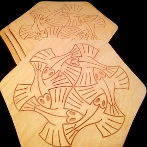 May include: A stack of hexagonal wooden coasters with a repeating etched design of stylized birds. The coasters are light brown with a dark brown etched pattern. The coasters are made of wood.