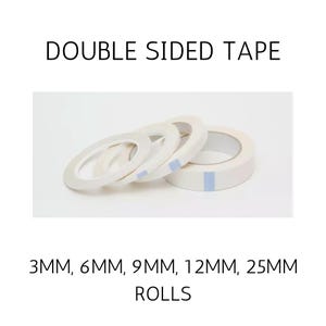 May include: Four rolls of white double sided tape arranged in a row. The text DOUBLE SIDED TAPE is at the top, and 3MM, 6MM, 9MM, 12MM, 25MM ROLLS is at the bottom. Each roll features a small blue rectangular tab on the outer edge.
